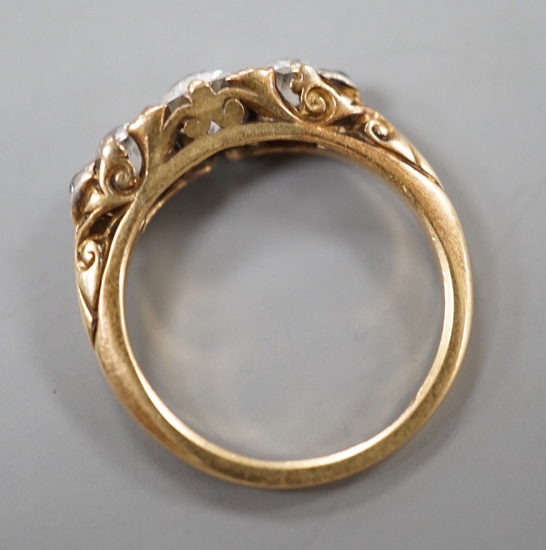 An early 20th century yellow metal and graduated three stone diamond ring, with diamond chip set shoulders, size J, gross weight 3 grams.